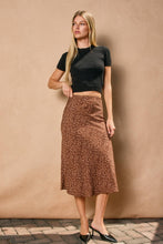 Load image into Gallery viewer, Woman wearing a black top and brown patterned skirt against a beige wall.