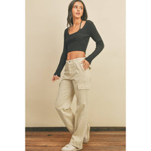 Load image into Gallery viewer, Woman wearing a black long-sleeve top and beige cargo pants against a beige wall.
