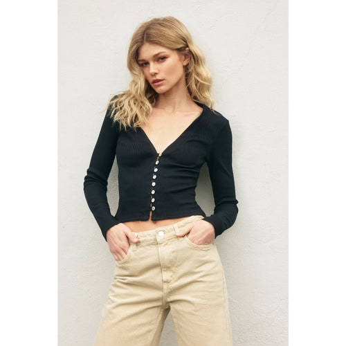 Woman wearing a black button-up top and beige pants against a light background