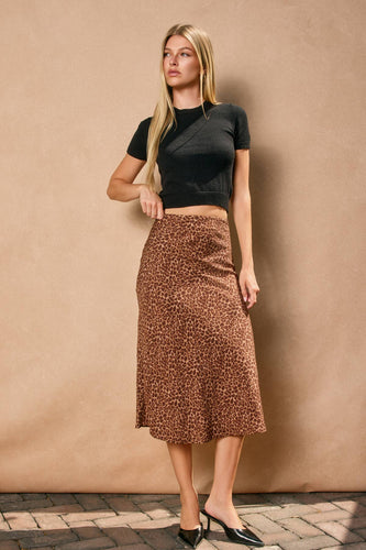 Woman wearing a black top and brown patterned skirt against a beige wall.