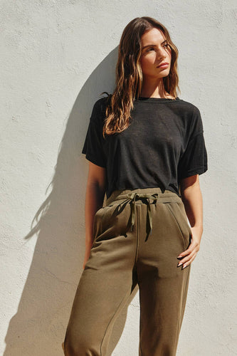 Woman wearing a black t-shirt and olive green pants against a gray wall